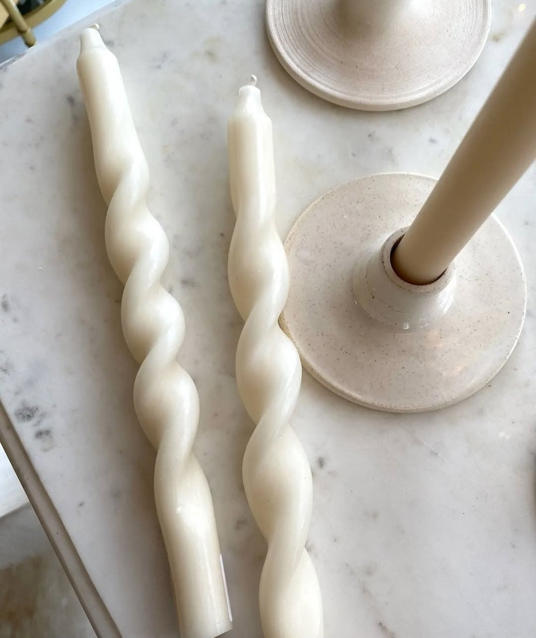 Twisted candles on a marble surface with a decorative holder.