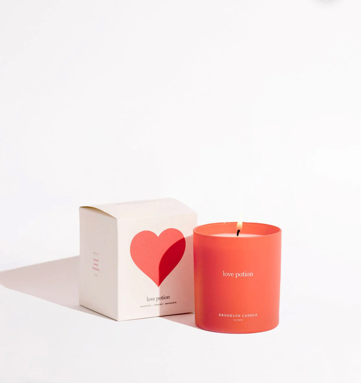 Coral candle with 'love potion' text next to a white box with a red heart on a light beige background